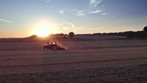 Tractor Cruising Through a Field Under the Golden Rays of the Setting Sun Stock Footage 240571551