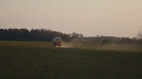 Tractor distributing fertilizer on field in sunset Vídeo Stock 153336980