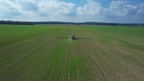 A tractor drives across a field, spraying fertilizer on a large field next to Stock Footage 233545934