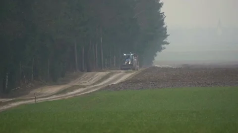 The tractor drives along the dirt road next to the forest and fields Stock Footage 237988357
