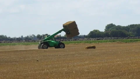 A tractor drives through a field collecting hay into bales. Video stock 329557725