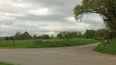Tractor drives through quiet county lanes on dull cloudy day in England Stock Footage 74699744
