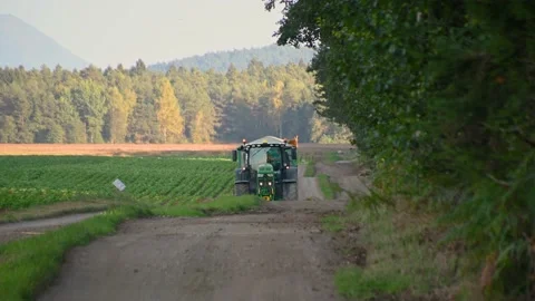 The tractor is driving along the countryside path next to the forest Stock Footage 226348459
