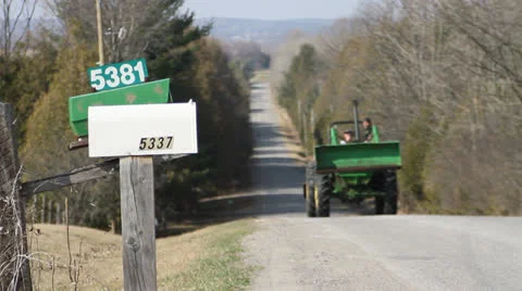 Tractor driving up steep hill on old country road by two mailboxes. 1080p 24. Stock Footage 22774253