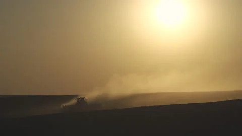 Tractor in the dust working in the field at sunset.  Vidéo 132104664