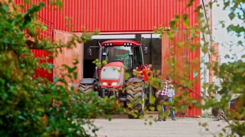 Tractor exiting red barn as people assist near farm entrance outdoors Stock Footage 333677247