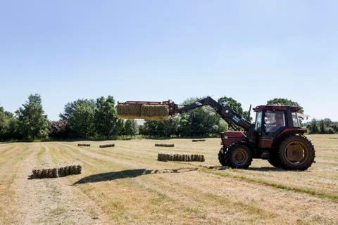 Tractor in a field, lifting stack of hay bales. Stockfoto's