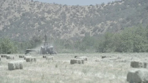 TRACTOR IN A FIELD MAKING HAY WITH MOUNTAINS IN THE BACK SLOW MOTION FARM GREEN Stock Footage 100776054