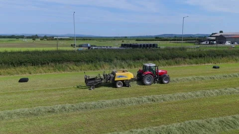 Tractor in field preparing hay bales for collection in an English countryside Stock Footage 293575859