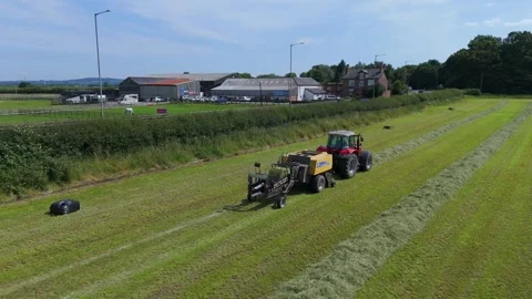Tractor in field preparing hay bales for collection in English countryside Stock Footage 293587138