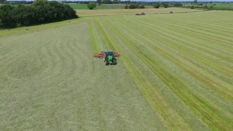 Tractor in field preparing hay bales for collection in English countryside Stock Footage 293587909