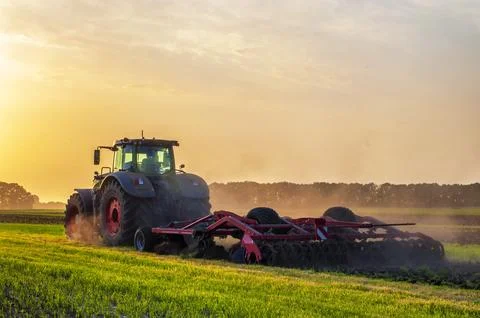 Tractor in the field under sunset light, tillage in spring Stock Photos