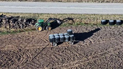 Tractor with front loader stacking silage bales on a trailer in a field, aerial Video stock 336289783