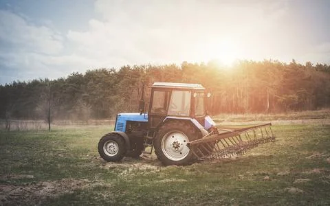 The tractor goes and pulls a plow plowing a field before landing of crops. Stock Photos
