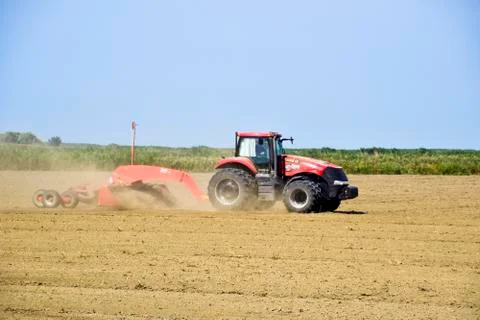 Tractor with a grader aligns the soil on the field. The tractor raised dust. Stock Photos
