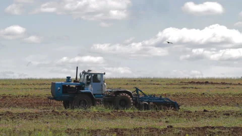 Tractor with harrow system plowing ground on cultivated farm field, pillar of Stock Footage 150630388