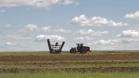 Tractor with harrow system plowing ground on cultivated farm field, pillar of Stock Footage 153508348