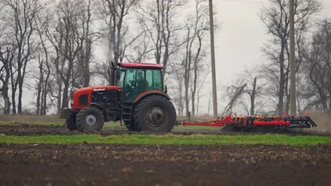 Tractor with harrow system plowing ground on cultivated farm field, pillar of Stock Footage 192911571