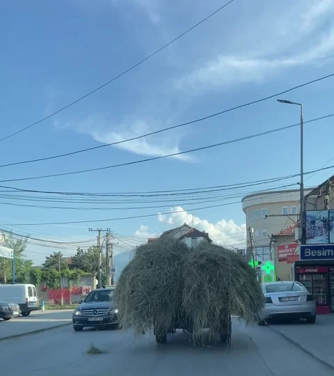 Tractor hauling large hay bale down busy city street, urban panning shot 库存影片 196980403