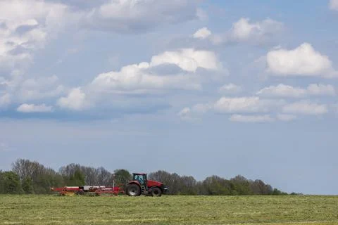 A tractor with hay tedder turning the grass cuttings in the meadow Stock Photos