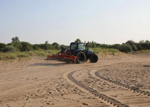 Tractor with large rake attached to the rear for morning beach maintenance .. Fotos Stock