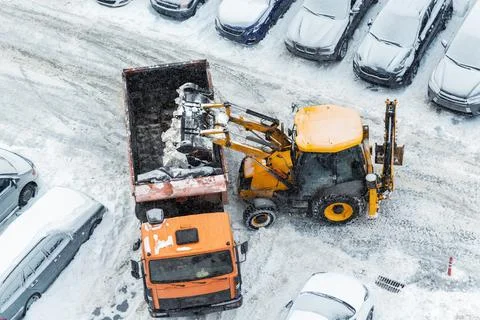 Tractor loader machine uploading dirty snow into dump truck. Cleaning city Stock Photos
