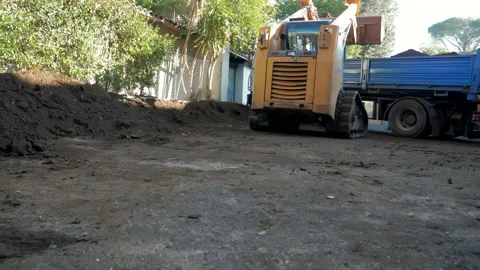 A tractor loader is picking up some soil with a large bucket and loading it to Stock Footage 148919341