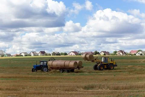 A tractor loading round hay bales on to a trailer Stock Photos