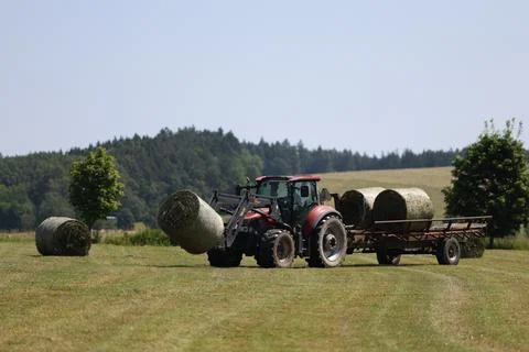 Tractor loading round hay bales onto a trailer on a summer field Stock Photos