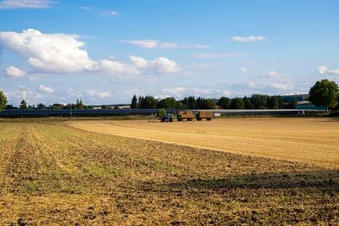 Tractor loading straw onto a trailer, on a harvested field Stock Photos