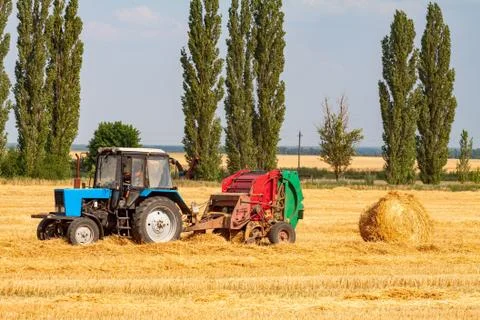 Tractor makes big straw roll on yellow field at summer day Stock Photos