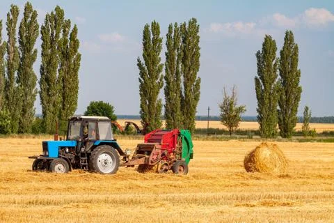 Tractor makes big straw roll on yellow field at summer day Stock Photos