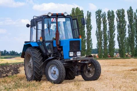 Tractor makes big straw roll on yellow field at summer day Stock Photos
