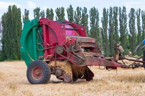 Tractor makes big straw roll on yellow field at summer day Stock Photos