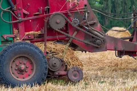 Tractor makes big straw roll on yellow field at summer day Stock Photos