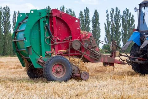 Tractor makes big straw roll on yellow field at summer day Stock Photos
