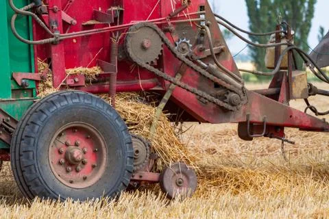 Tractor makes big straw roll on yellow field at summer day Foto stock