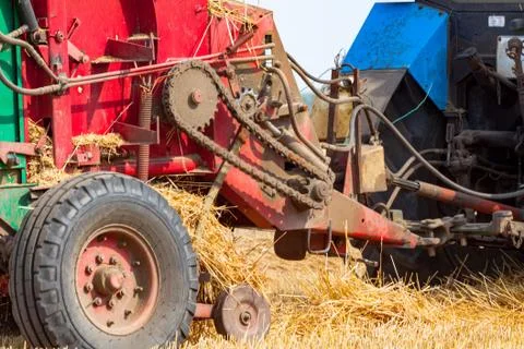 Tractor makes big straw roll on yellow field at summer day Stock Photos