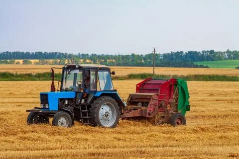 Tractor makes big straw roll on yellow field at summer day Stock Photos