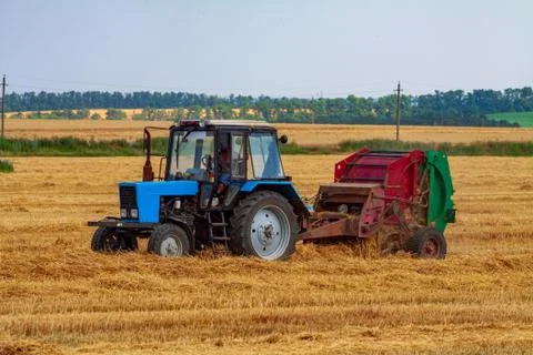 Tractor makes big straw roll on yellow field at summer day Stock Photos