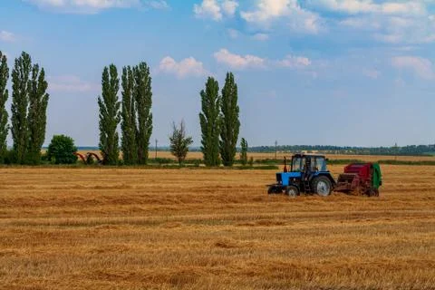 Tractor makes big straw roll on yellow field at summer day Stock Photos