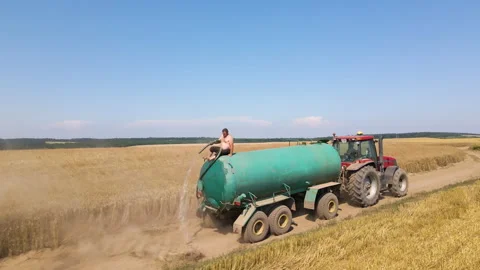 Tractor with man sitting on top of tank trailer sprinkling water against dust Stock Footage 308412851