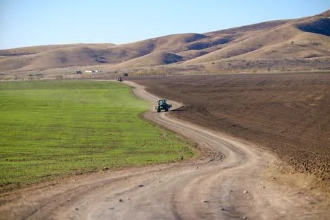 A tractor moves along the path beneath rolling hills and a clear blue sky 写真素材