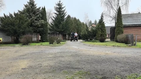 Tractor moves through rural area with trees and buildings in background on a gra Stock Footage 329408200