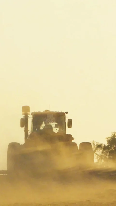 Tractor moving away across field through dust cloud at sunset with agricult.. Stock Footage 337444827
