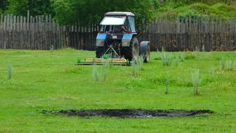 Tractor mows grass in a field near a wooden fence at a rural location Stock Footage 337452252