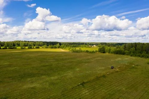 A tractor mows grass in a large field on a sunny summer day. Stock Photos