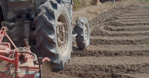 A tractor operates a rotary tiller to create planting rows in farmland. Stock Footage 323344081