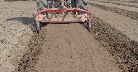 A tractor operates a rotary tiller to create planting rows in farmland. Stock Footage 323344171