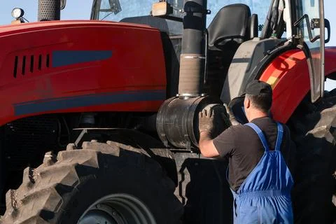A tractor operator farmer takes out or installs an air filter in his tracto.. Photos